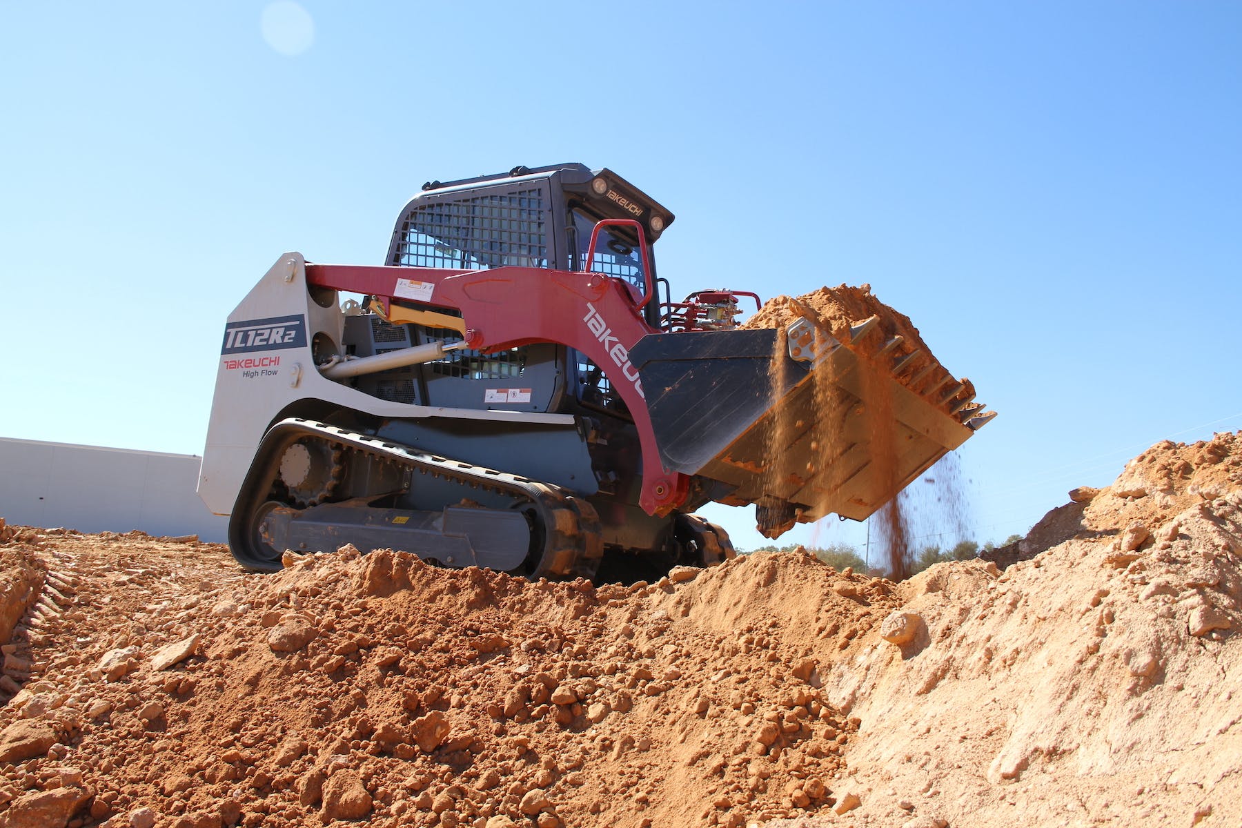 Takeuchi TL12R2 compact track loader side view above dirt hole hauling dirt in bucket