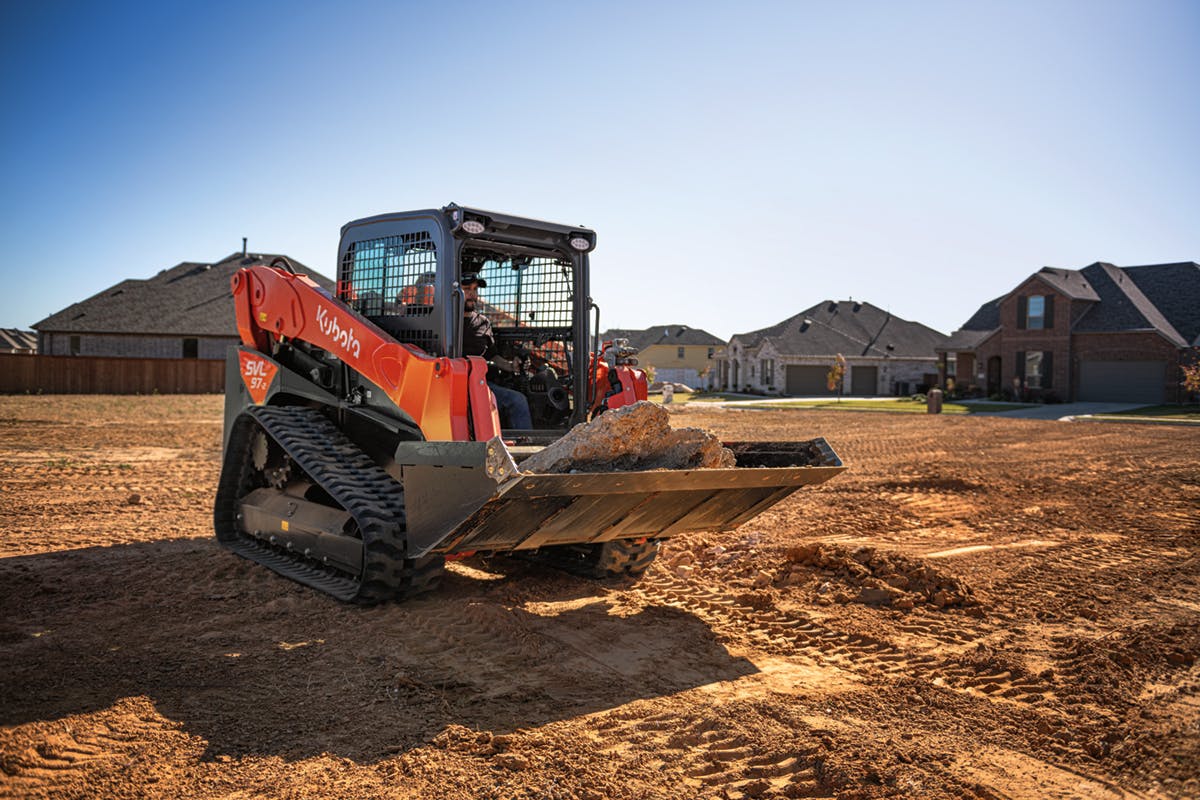 Kubota SVL97-2 compact track loader hauling concrete fragments in bucket over dirt grounds