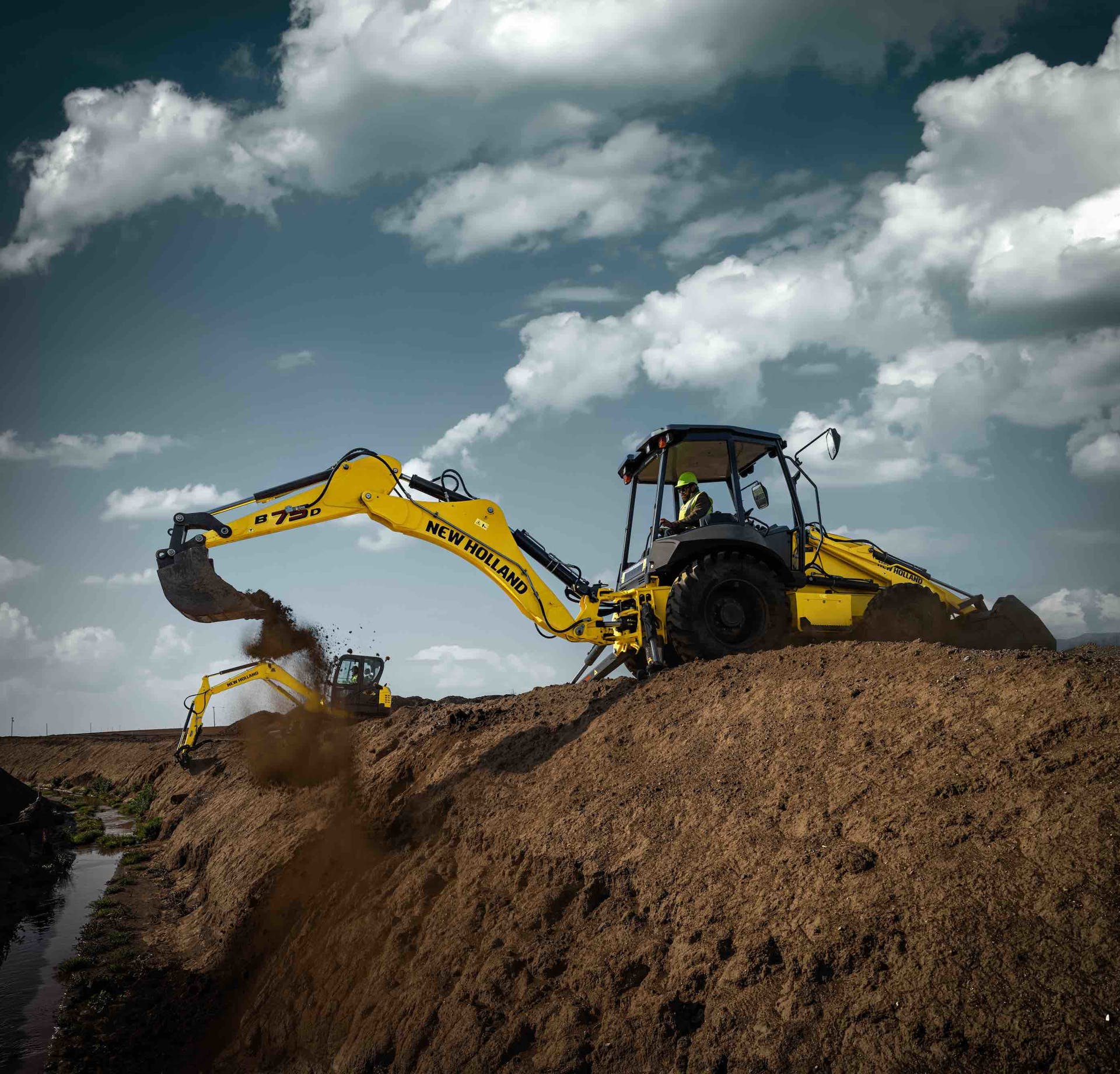 New Holland B75D backhoe on top of deep excavation dumping dirt